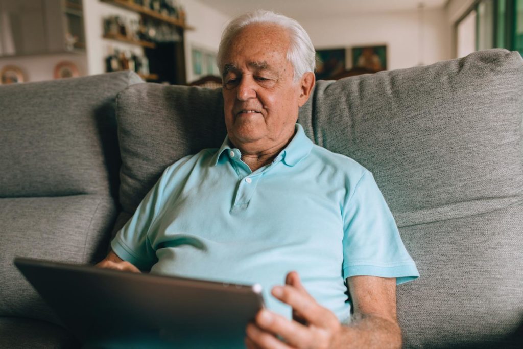 Older man in a blue polo enjoying leisure time with a tablet at home.