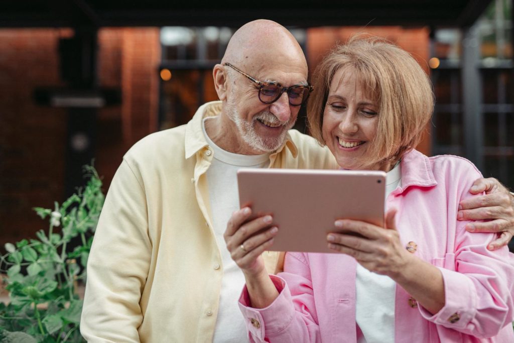 Happy senior couple using a tablet together, enjoying outdoor leisure time.